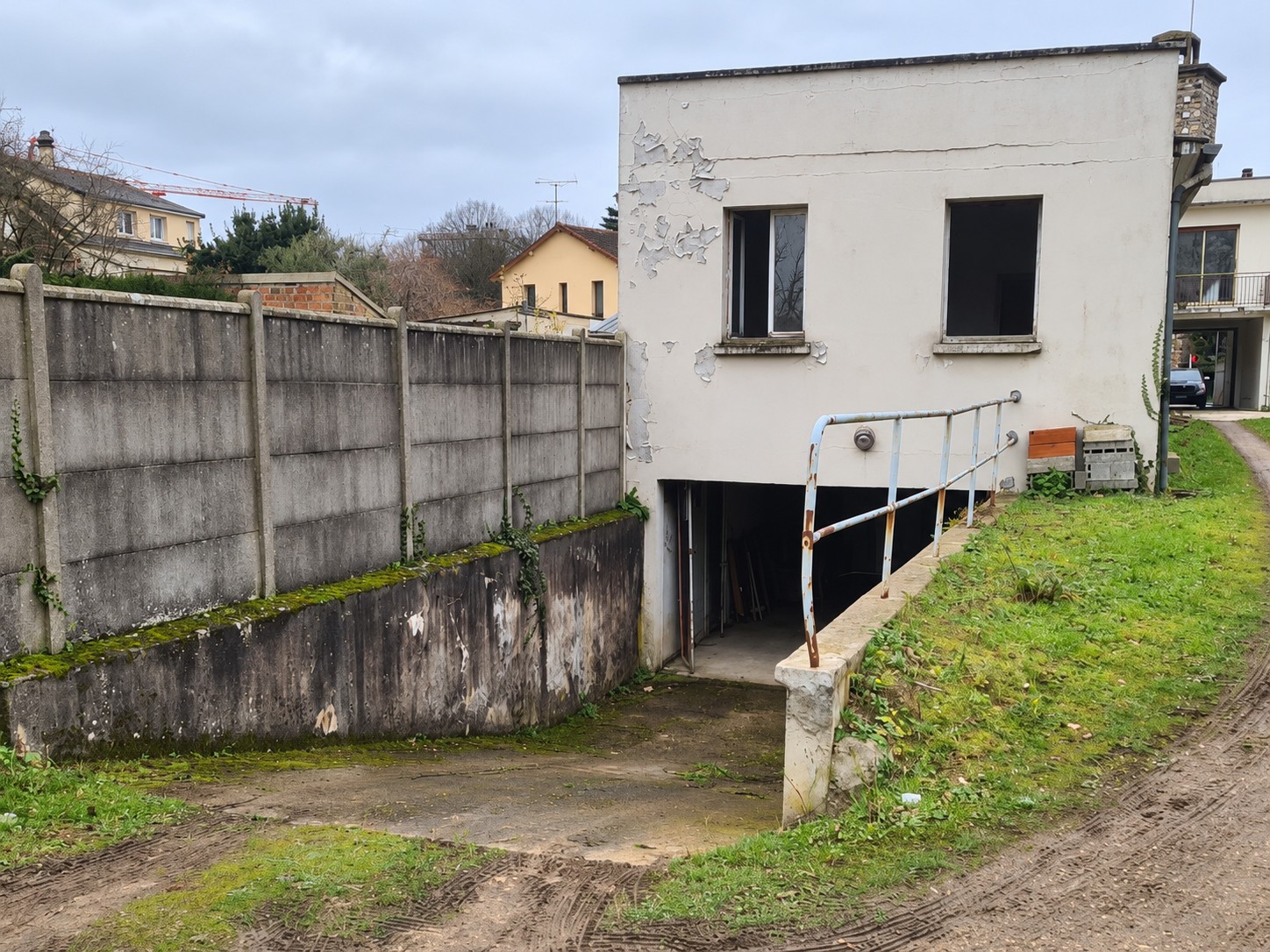 Vue de l’ancien abattoir à Ris-Orangis, avec façade dégradée, ancienne rampe d’accès au sous-sol et mur de clôture en béton.
