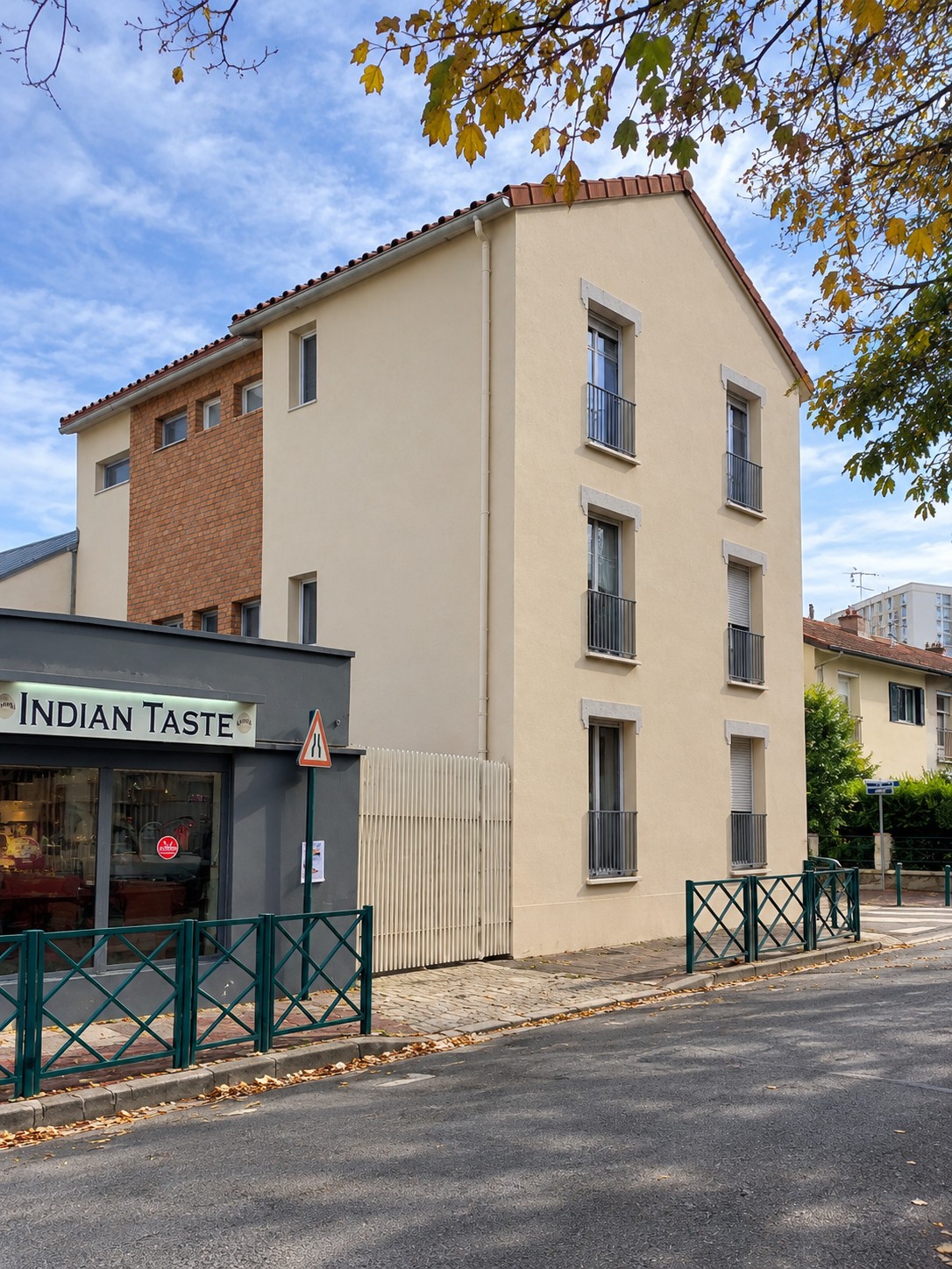 Façade projetée à Gennevilliers, avec enduit clair, brique et fenêtres sur trois niveaux, à côté d’un commerce.