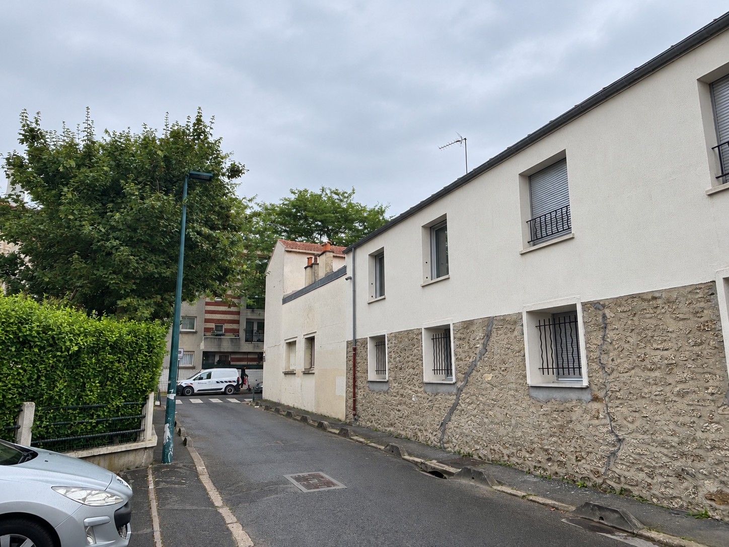 État existant depuis la rue latérale à Gennevilliers, avec façade basse en enduit clair, soubassement en pierre et fenêtres à barreaux.