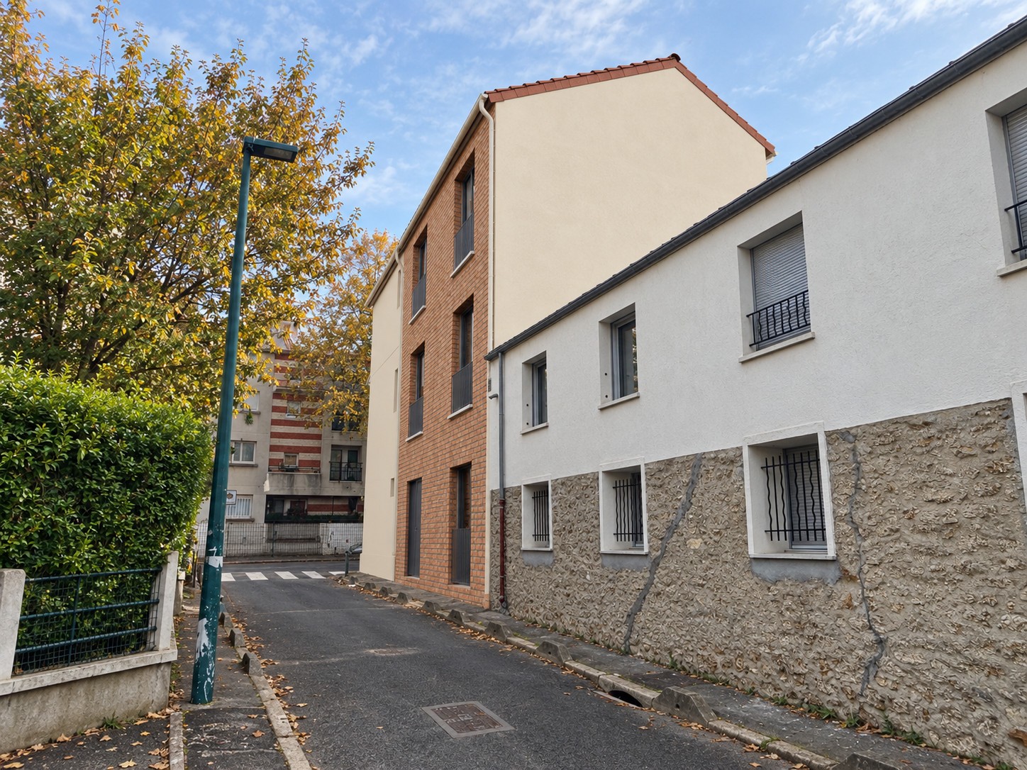 Projet de surélévation à Gennevilliers vu depuis la rue latérale, avec façade en brique et pignon clair près d’un bâtiment bas.
