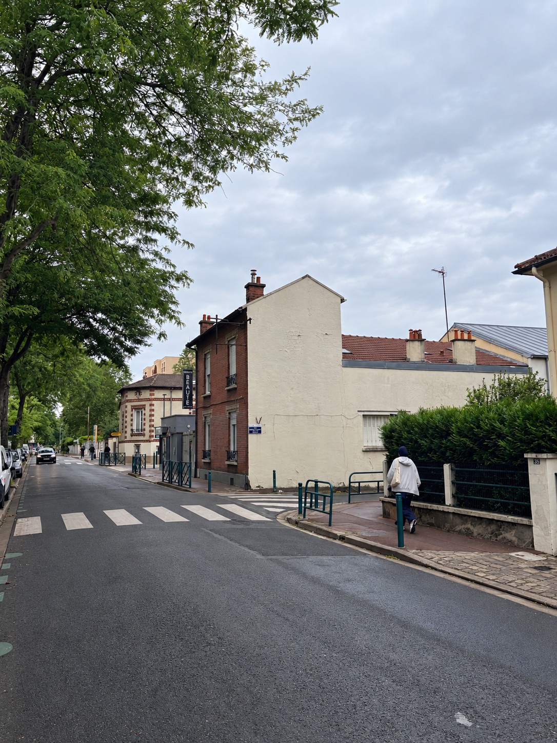 Bâtiment existant à Gennevilliers vu depuis l’angle de la rue, avec pignon clair, façade en brique et passage piéton.